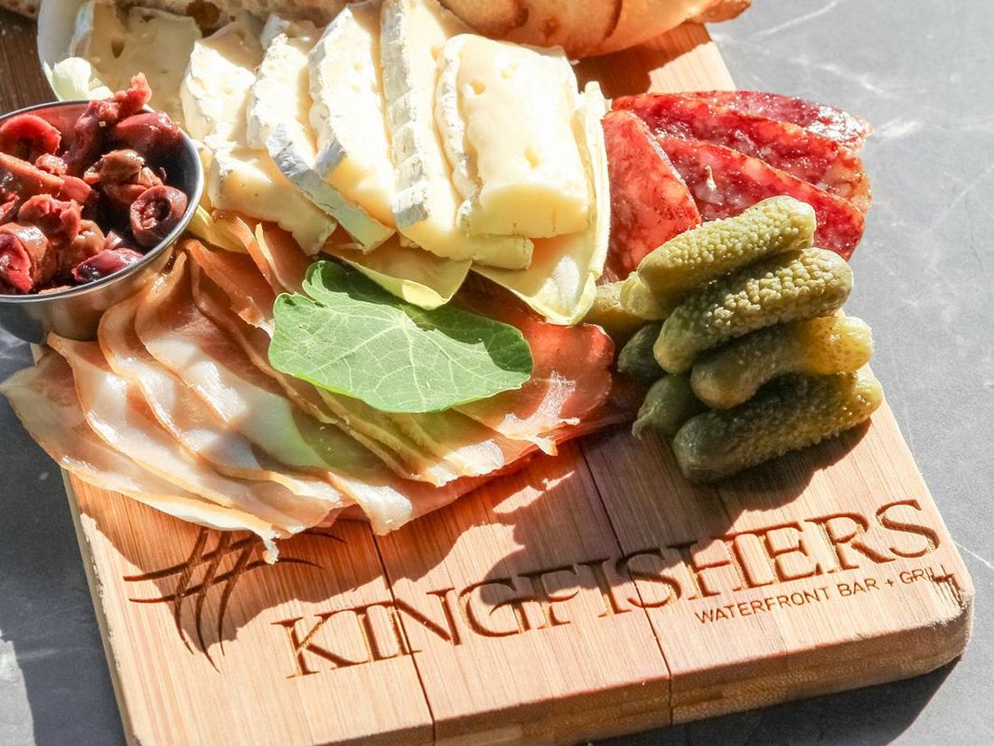 Charcuterie board with cured meats, brie, olives and pickles on a branded Kingfishers board